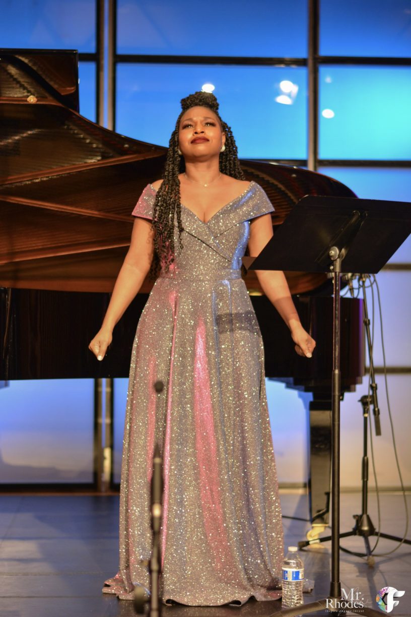 Stephanie Ann Ball, Soprano, in a floor-length sparkly gown performing in front of a grand piano.